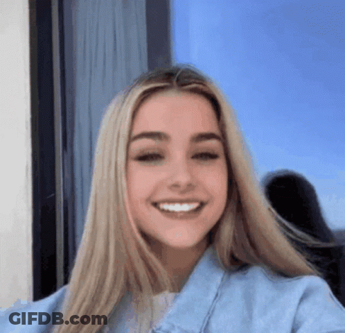A Woman With Long Blonde Hair Is Smiling For The Camera While Wearing A Blue Denim Jacket . GIF