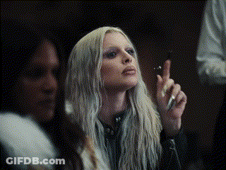 A Woman With Long Blonde Hair Is Smoking A Cigarette In A Dark Room GIF