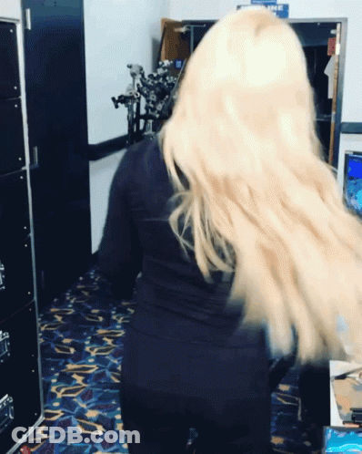 A Woman With Long Blonde Hair Is Standing In A Room With A Sign That Says Airline GIF