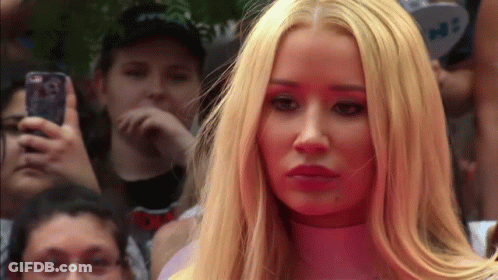 A Woman With Long Blonde Hair Is Standing In Front Of A Crowd While A Man Takes A Picture With His Phone GIF