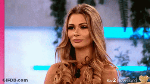 A Woman With Long Blonde Hair Is Standing In Front Of A Love Island Sign GIF