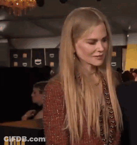A Woman With Long Blonde Hair Is Standing In Front Of A Table And Looking At Something . GIF
