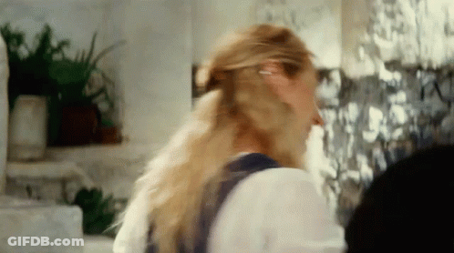 A Woman With Long Blonde Hair Is Standing In Front Of A Wall With Pictures On It GIF