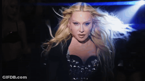 A Woman With Long Blonde Hair Is Standing In The Dark GIF