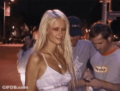 A Woman With Long Blonde Hair Is Standing Next To A Man In A Gray Shirt . GIF