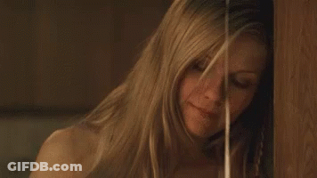 A Woman With Long Blonde Hair Is Standing Next To A Wooden Wall . GIF