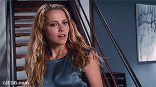 A Woman With Long Blonde Hair Is Standing On A Set Of Stairs Looking At The Camera GIF