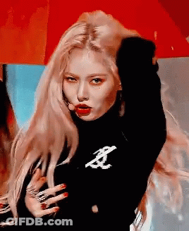 A Woman With Long Blonde Hair Is Wearing A Black Turtleneck Sweater And Red Lipstick . GIF
