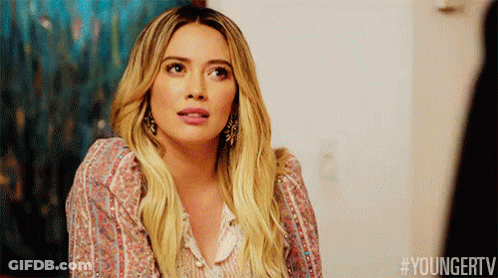 A Woman With Long Blonde Hair Is Wearing A Floral Shirt And Earrings And Making A Funny Face . GIF