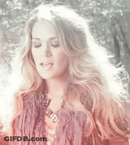 A Woman With Long Blonde Hair Is Wearing A Fringed Jacket And A Necklace GIF
