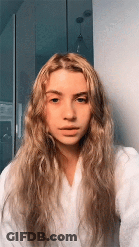 A Woman With Long Blonde Hair Is Wearing A White Robe And Taking A Selfie GIF
