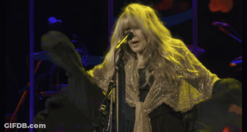 A Woman With Long Blonde Hair Singing Into A Microphone On A Stage GIF