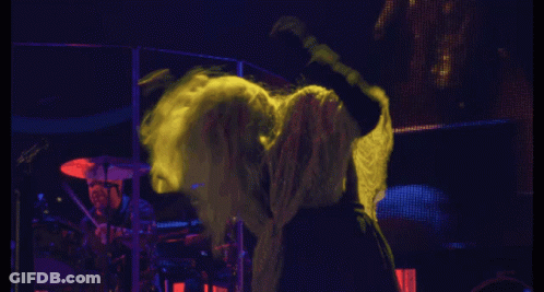 A Woman With Long Blonde Hair Stands In Front Of A Drummer On A Stage GIF