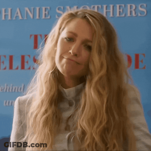 A Woman With Long Blonde Hair Stands In Front Of A Sign That Says Hanie Smothers GIF