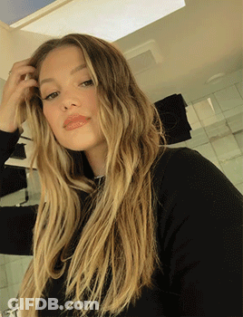 A Woman With Long Blonde Hair Wearing A Black Sweater GIF