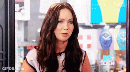 A Woman With Long Brown Hair And Blue Eyes Is Sitting In Front Of A Mtv Seven Sign . GIF