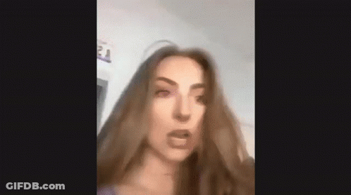 A Woman With Long Brown Hair Is Making A Funny Face And Looking At The Camera . GIF
