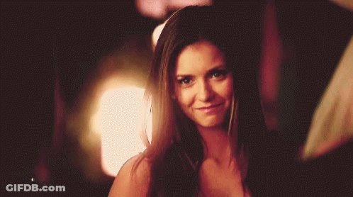 A Woman With Long Brown Hair Is Smiling And Looking At The Camera . GIF
