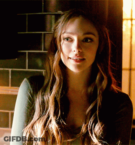 A Woman With Long Brown Hair Is Smiling In Front Of A Tiled Wall GIF
