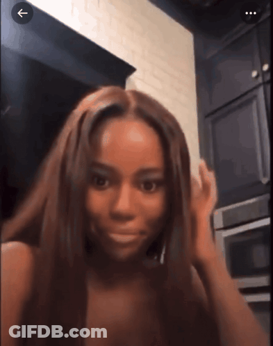 A Woman With Long Brown Hair Is Standing In A Kitchen With An Arrow Pointing To The Right GIF