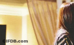 A Woman With Long Brown Hair Is Standing In Front Of A Curtain . GIF