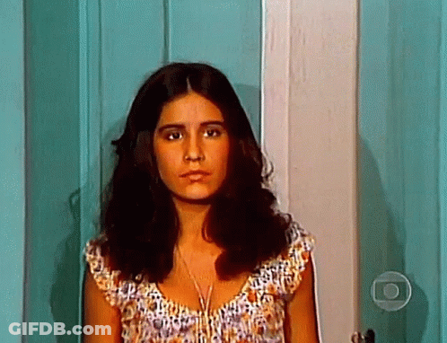 A Woman With Long Brown Hair Is Standing In Front Of A Door . GIF
