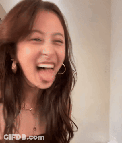 A Woman With Long Brown Hair Is Sticking Her Tongue Out And Laughing . GIF