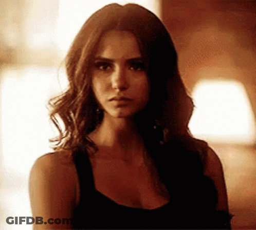 A Woman With Long Brown Hair Is Wearing A Black Tank Top And Looking At The Camera . GIF