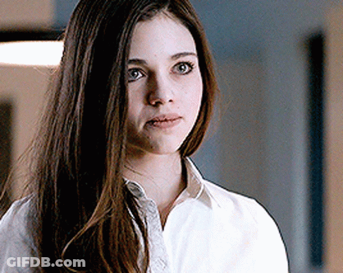 A Woman With Long Brown Hair Is Wearing A White Shirt And Looking At The Camera . GIF