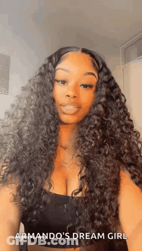 A Woman With Long Curly Hair And A Plunging Neckline Is Wearing A Black Tank Top . GIF