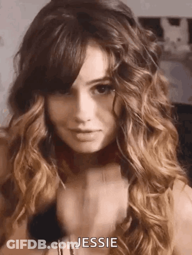 A Woman With Long Curly Hair And Bangs Is Wearing A Choker Necklace And Looking At The Camera . GIF