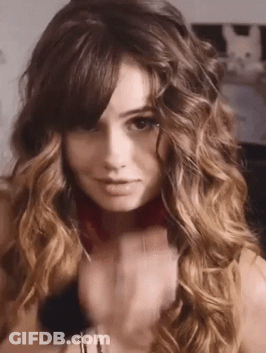 A Woman With Long Curly Hair And Bangs Is Wearing A Choker Necklace . GIF