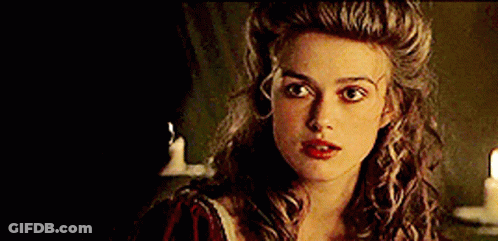 A Woman With Long Curly Hair And Red Lips Is Standing In Front Of A Candle . GIF