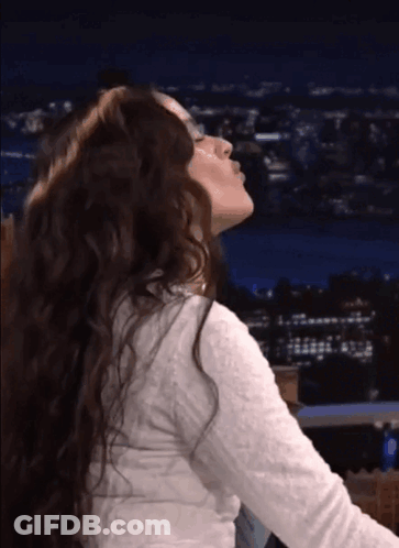 A Woman With Long Curly Hair Is Blowing A Kiss At Night GIF