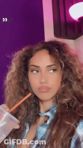 A Woman With Long Curly Hair Is Drinking A Drink With A Straw . GIF