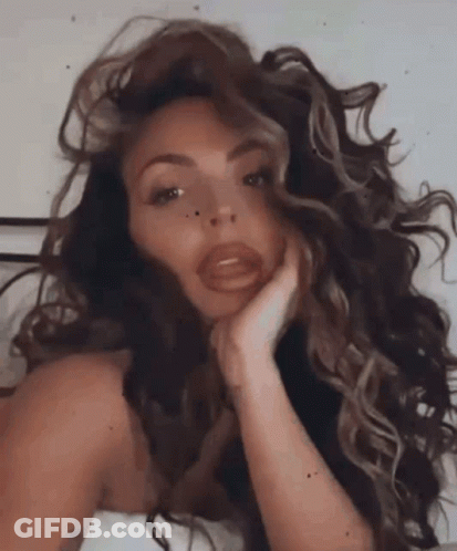 A Woman With Long Curly Hair Is Laying On A Bed With Her Hand On Her Chin . GIF