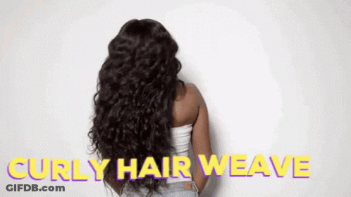 A Woman With Long Curly Hair Is Standing In Front Of A White Wall With The Words `` Curly Hair Weave '' Written On It . GIF