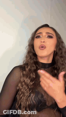 A Woman With Long Curly Hair Wearing A Black Top Is Making A Funny Face . GIF