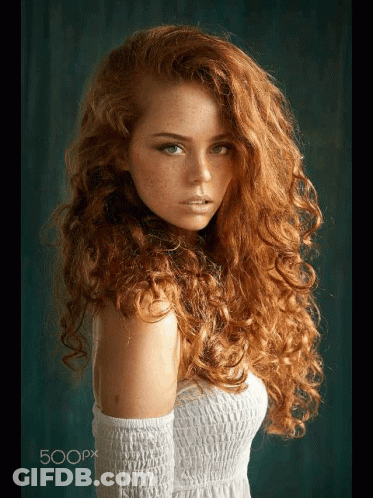 A Woman With Long Curly Red Hair And Freckles Is Wearing A White Dress GIF