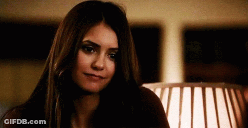 A Woman With Long Dark Hair Is Sitting In Front Of A Lamp And Looking At The Camera . GIF