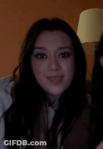 A Woman With Long Dark Hair Is Smiling And Looking At The Camera GIF