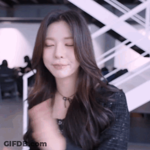 A Woman With Long Dark Hair Is Standing In Front Of A White Staircase . GIF