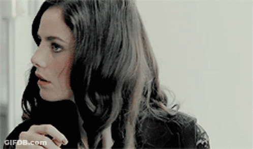A Woman With Long Dark Hair Is Wearing A Black Lace Top And A Black Turtleneck . GIF