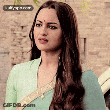 A Woman With Long Hair And A Bindi On Her Forehead Is Wearing A Blue Blouse And A Green Saree . GIF