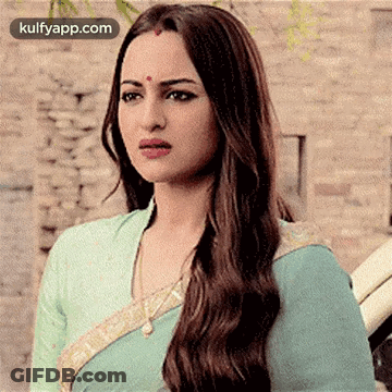 A Woman With Long Hair And A Bindi On Her Forehead Is Wearing A Blue Saree And Looking At The Camera . GIF