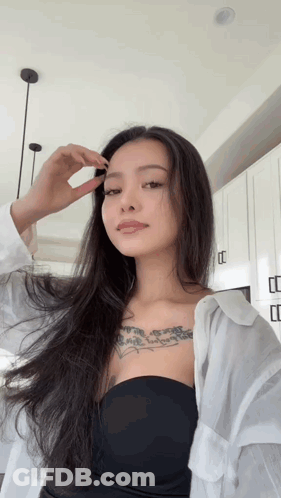 A Woman With Long Hair And A Tattoo On Her Chest Looks At The Camera GIF