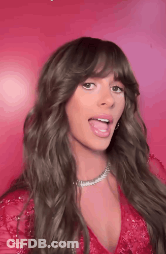 A Woman With Long Hair And Bangs Is Sticking Her Tongue Out In Front Of A Pink Background . GIF