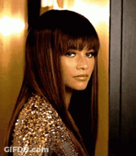 A Woman With Long Hair And Bangs Is Wearing A Gold Sequined Dress . GIF