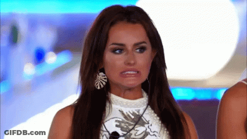 A Woman With Long Hair And Earrings Is Making A Funny Face While Standing In Front Of A Microphone . GIF
