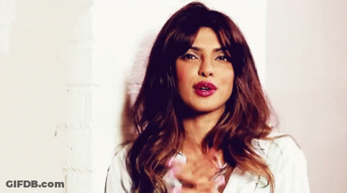 A Woman With Long Hair And Red Lipstick Is Standing In Front Of A Wall . GIF